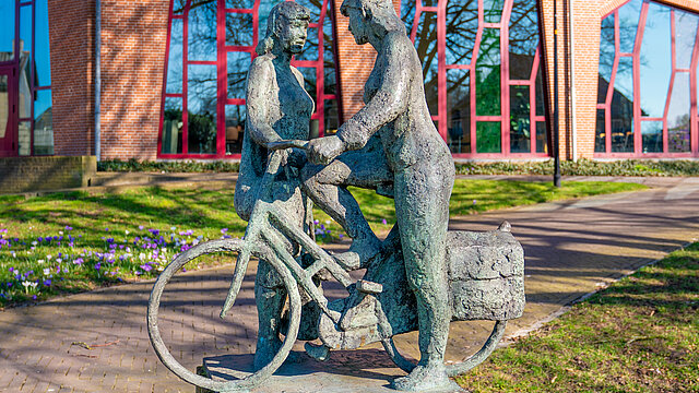 Foto van een standbeeld van een vrouw op de fiets voor het gemeentehuis